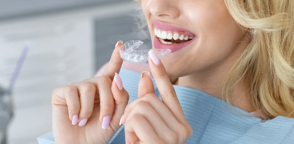 Smiling blonde woman holding a clear aligner for teeth straightening treatment at Clearly Dental Dapto.